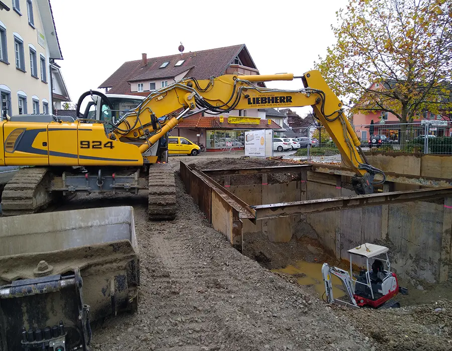 Bagger arbeitet an einer gesicherten Baugrube im innerstädtischen Bereich